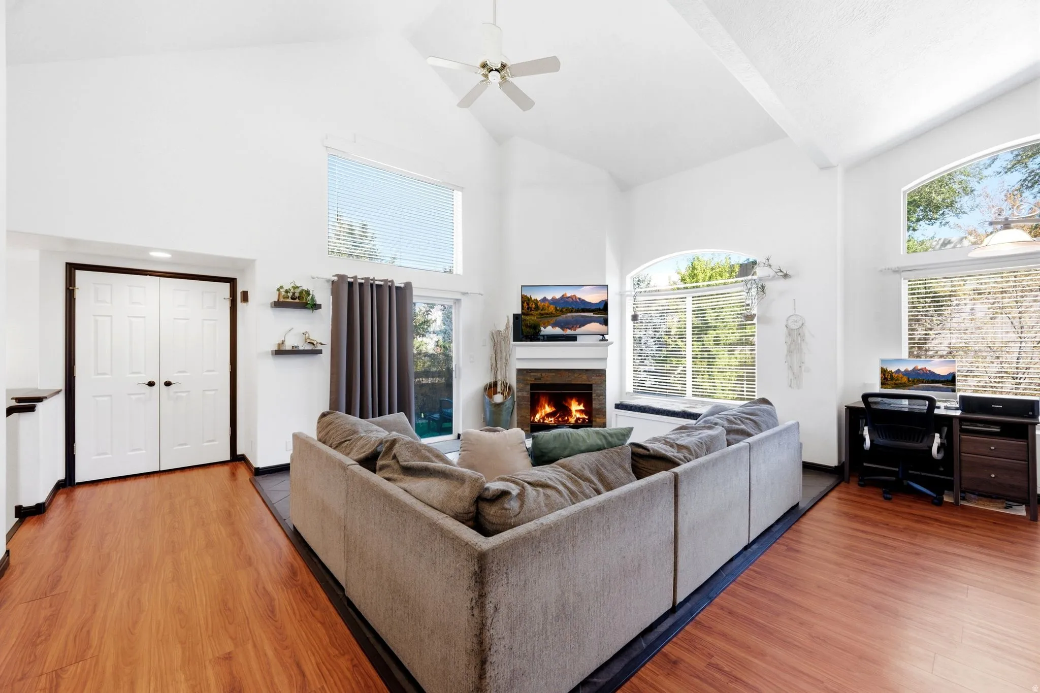 Vaulted ceiling with a ceiling fan, wood-finish flooring, and a stone-clad fireplace