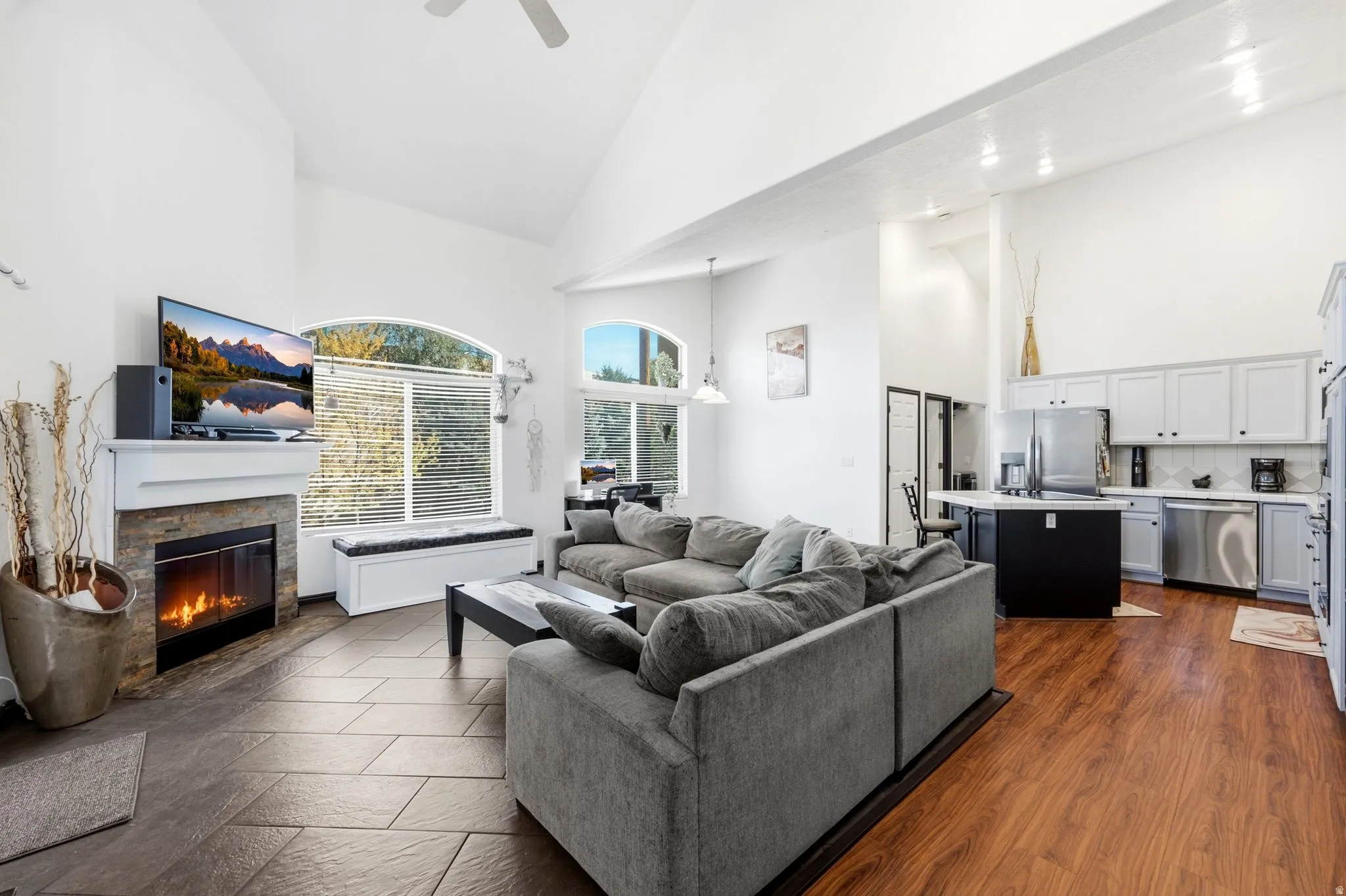 Vaulted ceilings with a ceiling fan, stone-clad fireplace, and an arched window
