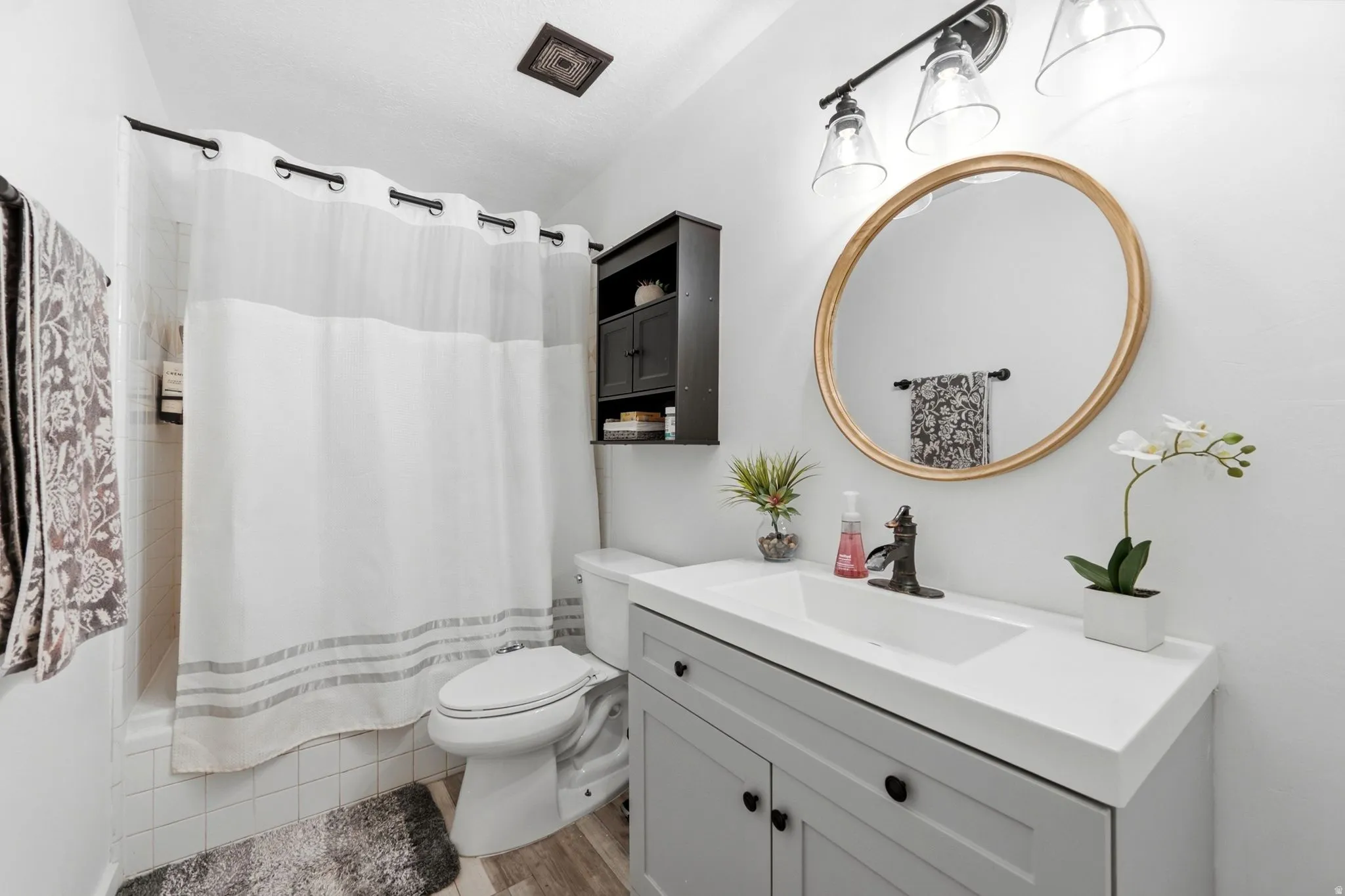Vanity with an integrated rectangular sink, gray base cabinetry, and a gold-framed circular mirror