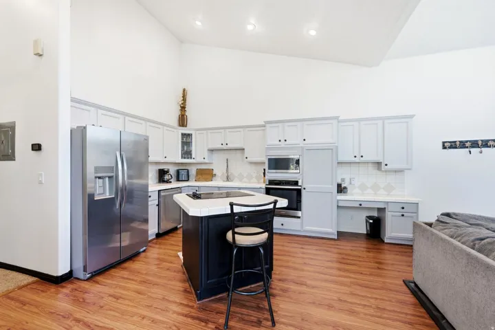 Vaulted ceiling, wood-finish flooring, stainless steel appliances, kitchen island with built-in cooktop, light-toned cabinetry