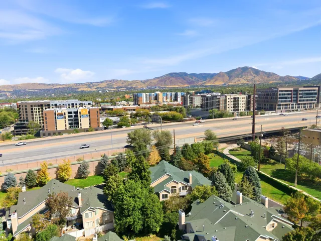 Expansive urban landscape with distant mountains, multiple residential and commercial structures, and a prominent highway