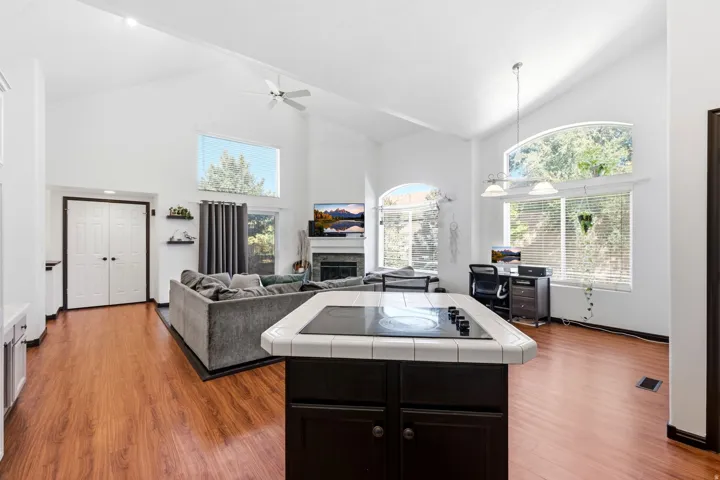 Vaulted ceilings, wood-finish flooring, fireplace, large windows, and an island with a built-in cooktop