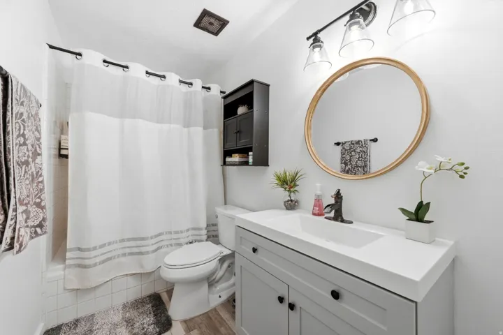 Vanity with an integrated rectangular sink, gray base cabinetry, and a gold-framed circular mirror