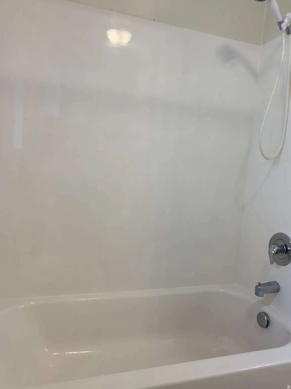 White bathtub with an integrated shower, featuring polished chrome fixtures and a handheld showerhead