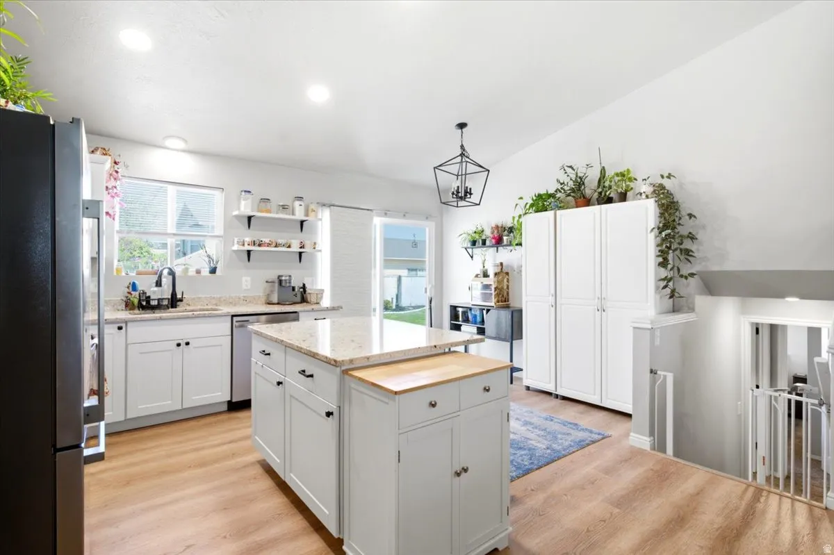 White shaker cabinetry, light wood-finish flooring, recessed lighting, kitchen island with stone countertop, and black appliances