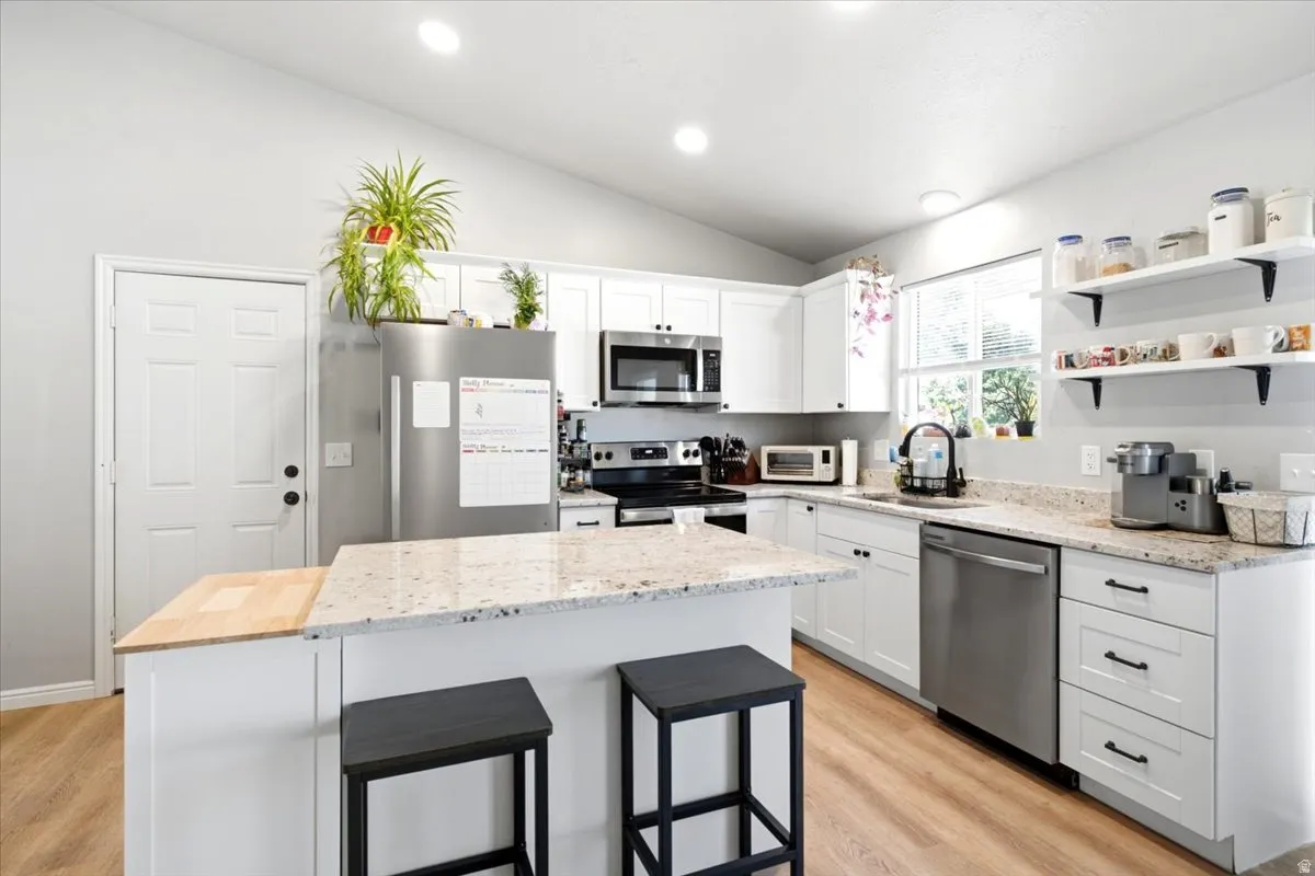 Bright kitchen featuring white cabinetry, light-toned countertops, stainless steel appliances, and wood-finish flooring