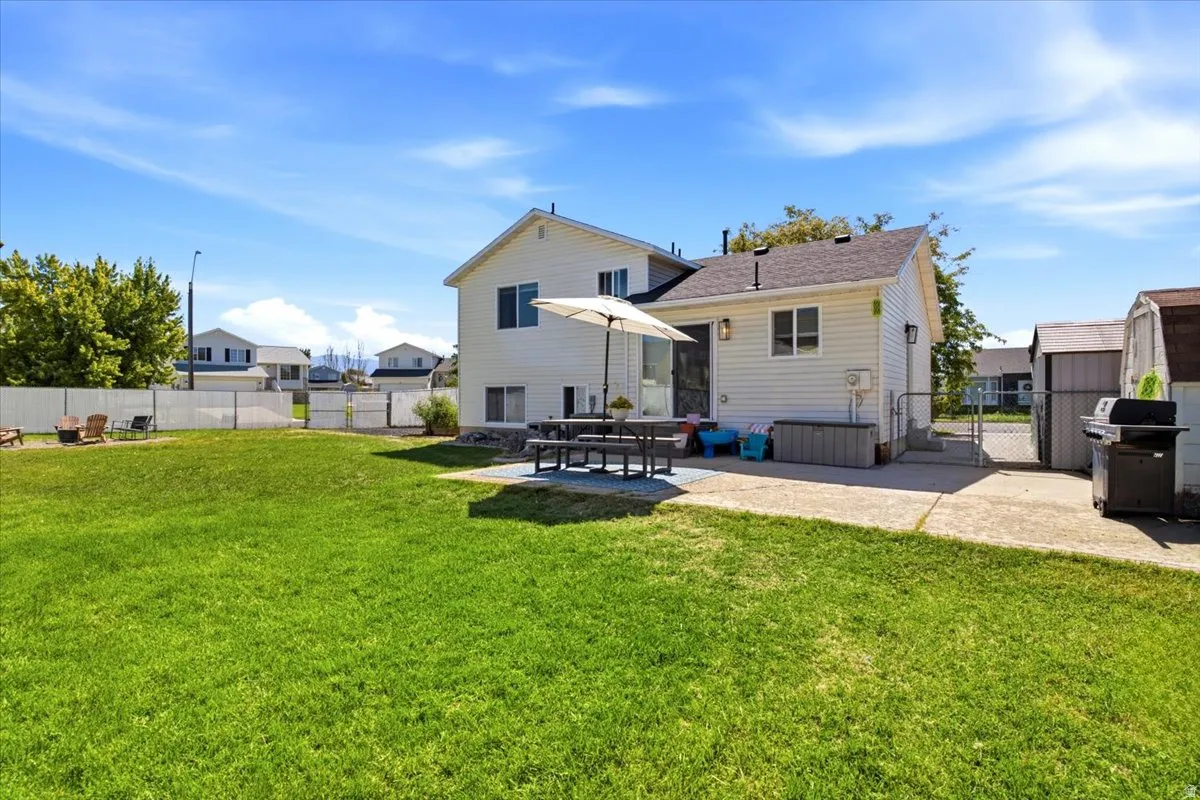 Expansive grass lawn with a white vinyl fence, concrete patio, and rear house elevation with white siding