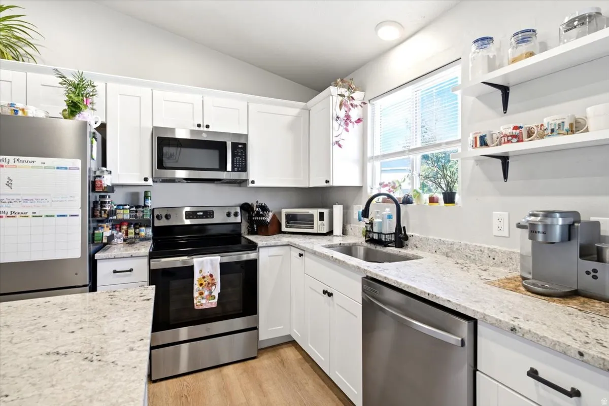 Modern kitchen featuring white shaker-style cabinetry, granite-style countertops, stainless steel appliances, and wood-finish flooring