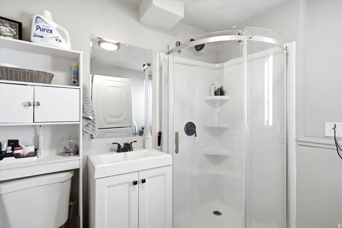 White vanity with integrated sink, curved glass shower enclosure, built-in shower shelving, and wall-mounted storage cabinetry
