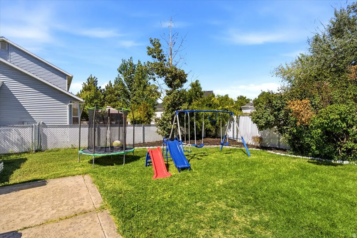 Expansive green lawn, established trees and shrubs, paved patio area, chain-link fencing, and a privacy fence