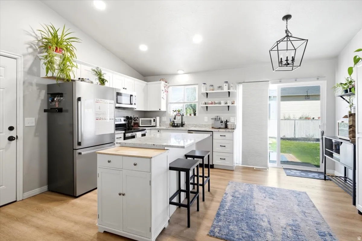 Vaulted ceiling with recessed lighting, white cabinetry, wood-finish flooring, stainless steel appliances, and a sliding glass door to the exterior