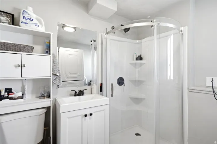 White vanity with integrated sink, curved glass shower enclosure, built-in shower shelving, and wall-mounted storage cabinetry