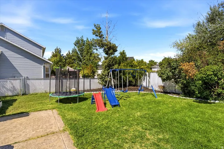 Expansive green lawn, established trees and shrubs, paved patio area, chain-link fencing, and a privacy fence