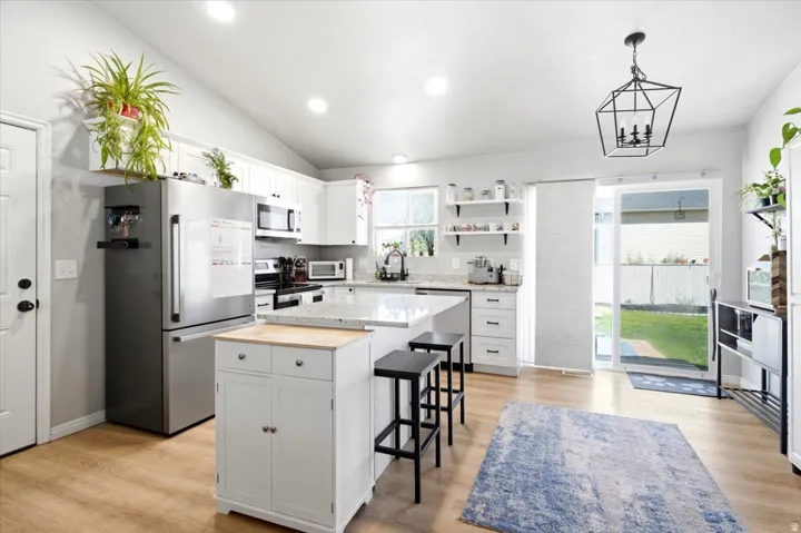 Vaulted ceiling with recessed lighting, white cabinetry, wood-finish flooring, stainless steel appliances, and a sliding glass door to the exterior