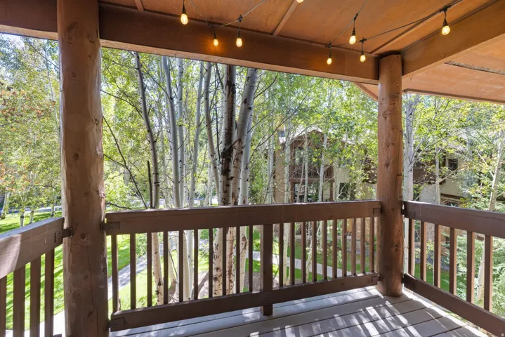Covered outdoor deck with string lighting, log columns, and wood railings