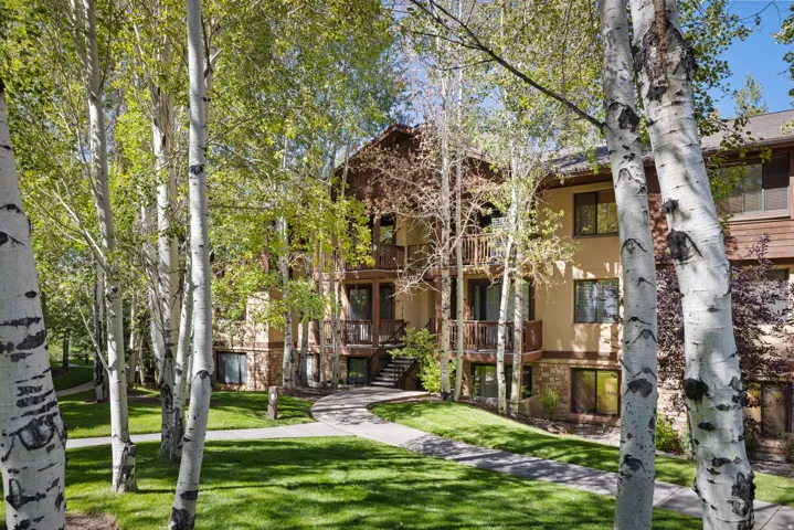 Stucco and stone exterior with multiple balconies, framed by numerous mature trees