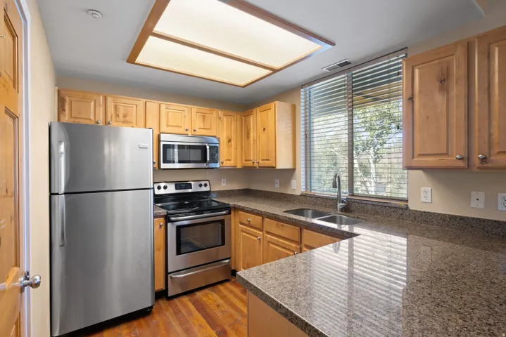 Kitchen featuring wood-finish cabinetry, stainless steel appliances, speckled countertops, and wood-finish flooring