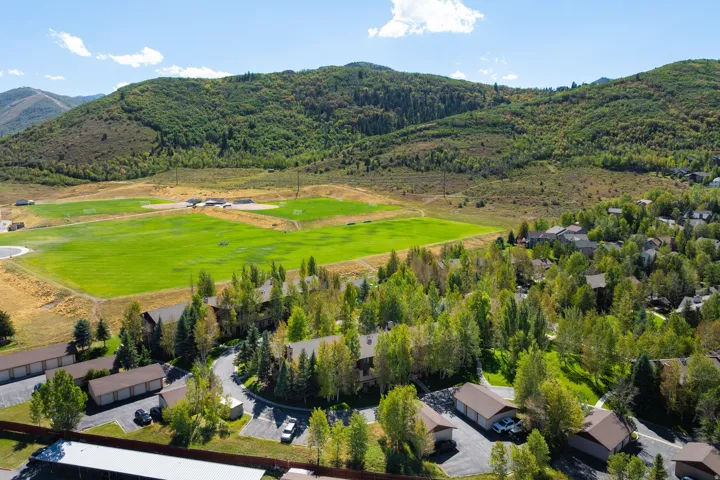 Mountainous terrain with natural vegetation, multiple sports fields, and residential properties with lush trees