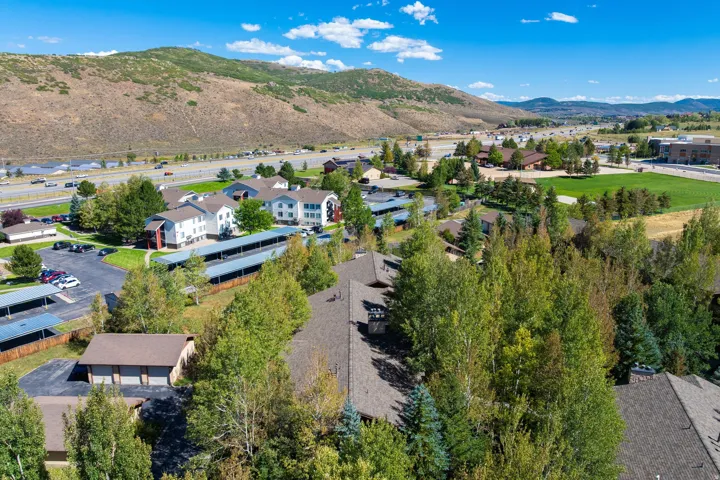 Expansive property featuring multiple residential buildings, covered parking structures, mature trees, and mountainous surroundings