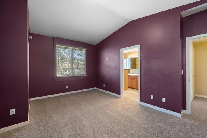 Vaulted ceiling room with neutral carpet, a single window, and two interior doorways