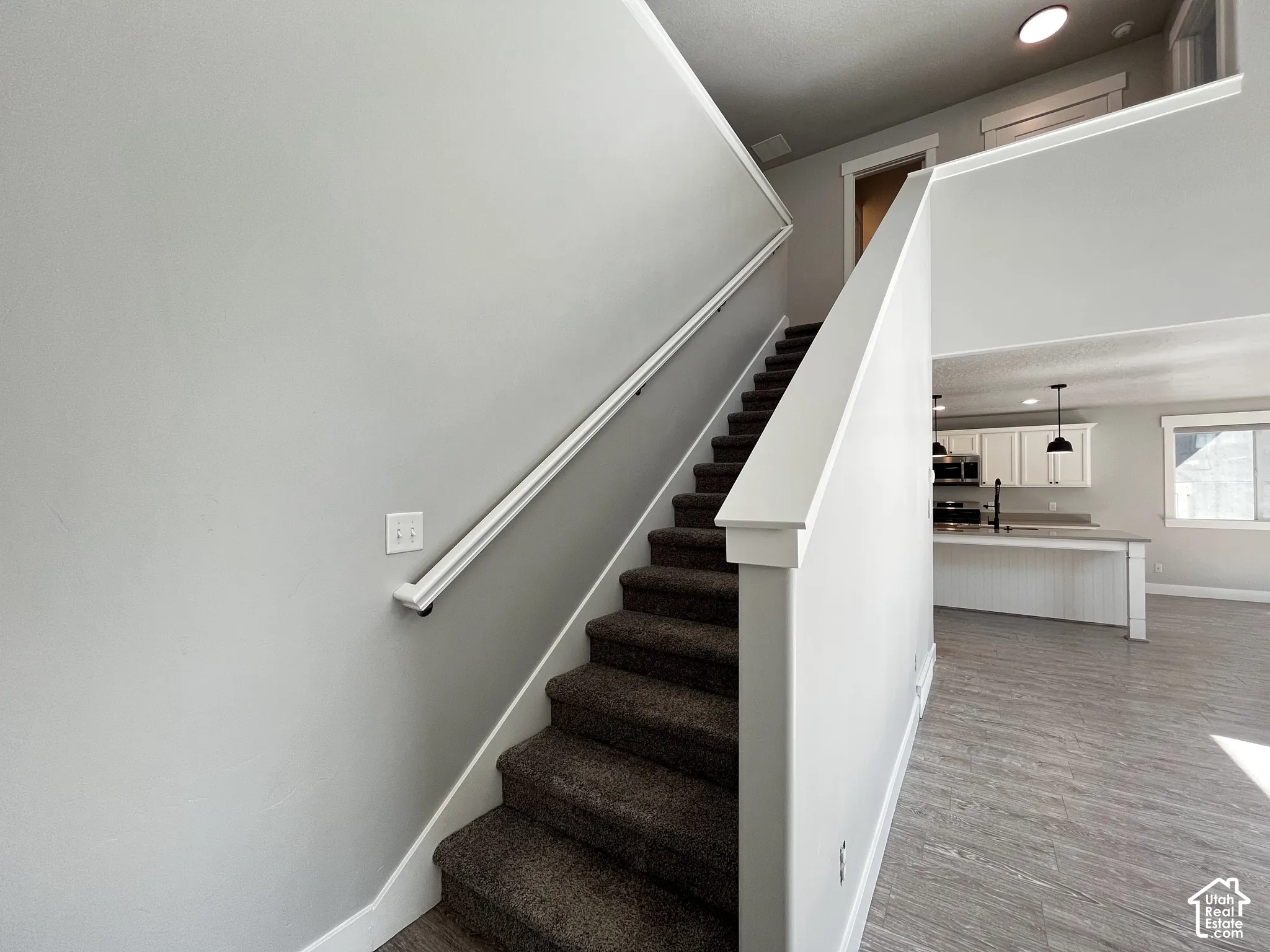 Carpeted staircase with white handrail, recessed lighting, wood-finish flooring, and white kitchen cabinetry