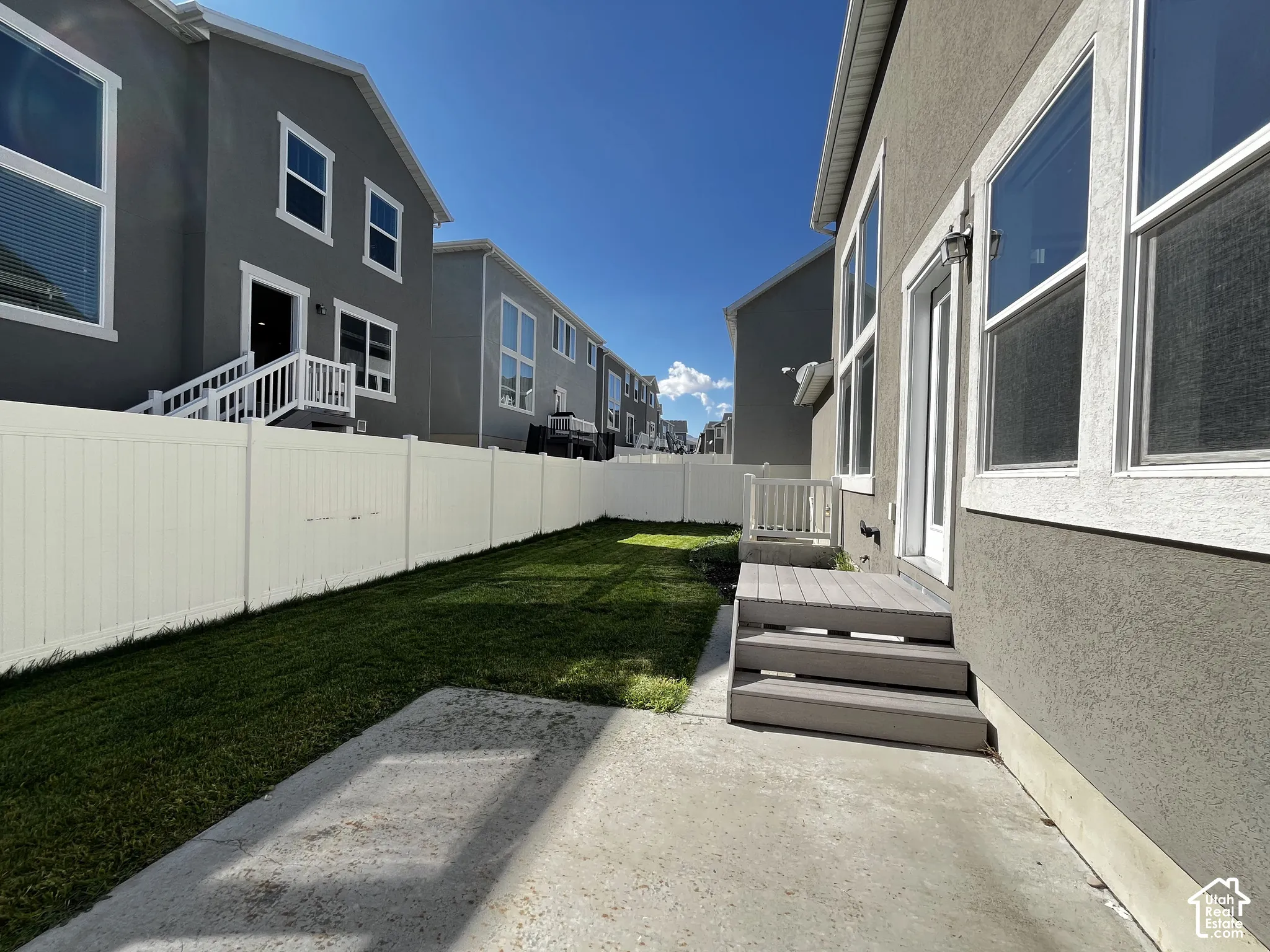 Expansive concrete patio with direct access to a private backyard, featuring a white privacy fence and a composite deck with steps