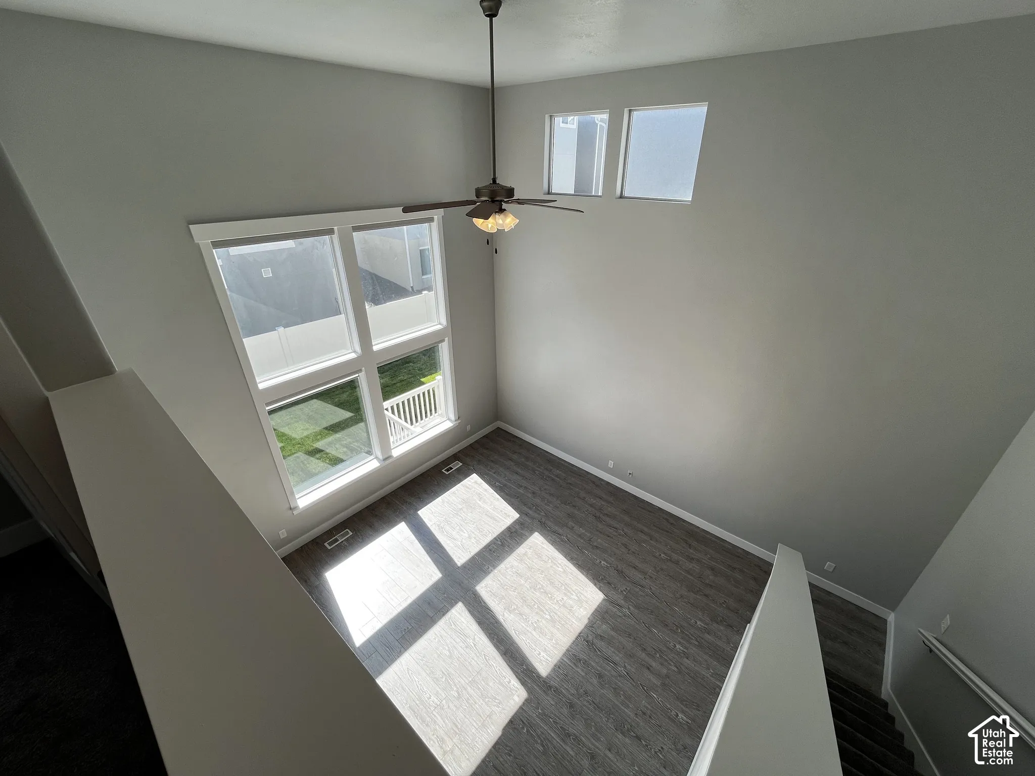 Double-height ceiling, large multi-pane windows, elevated windows, wood-finish flooring, and a ceiling fan with integrated lighting