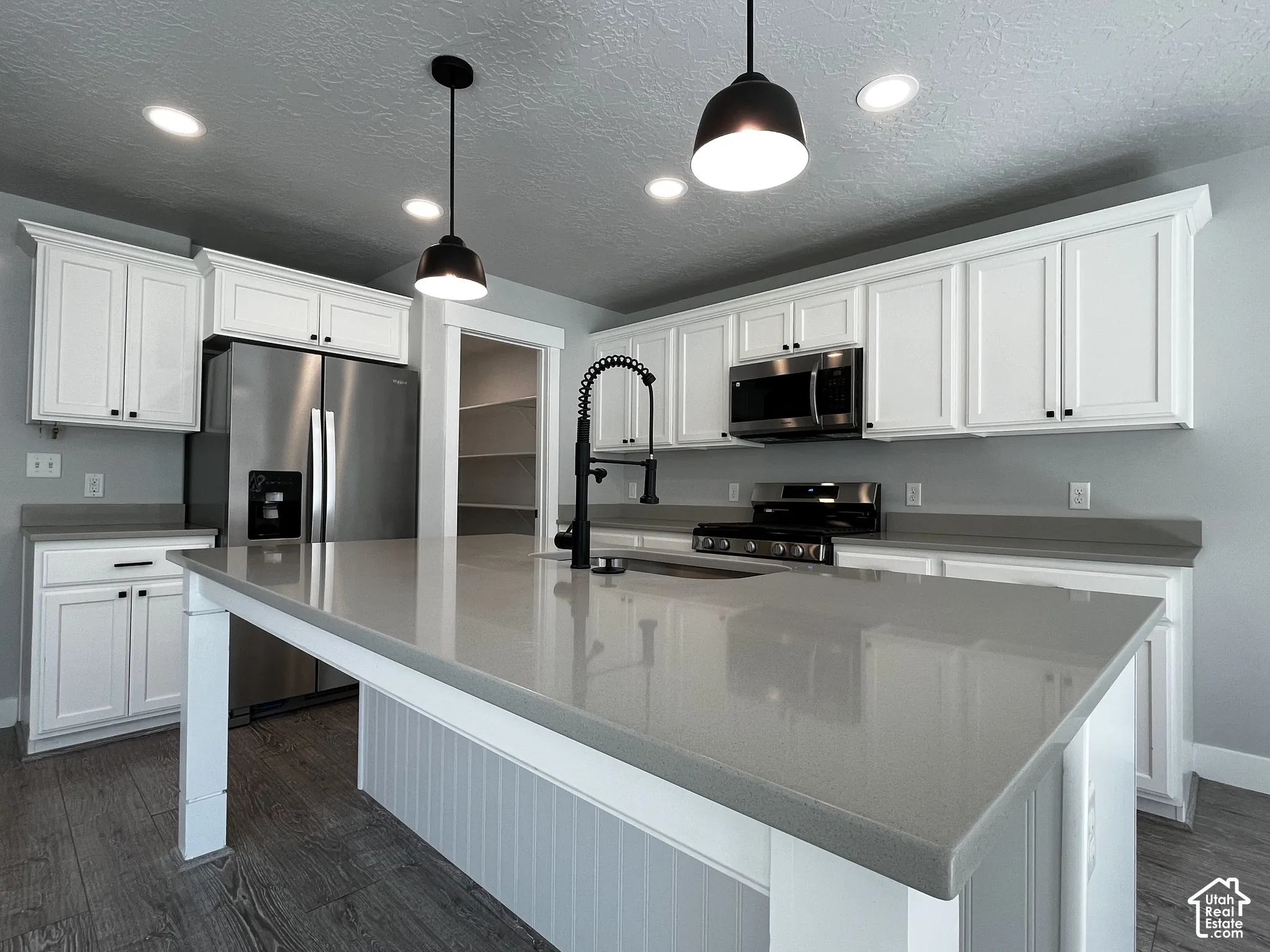 Kitchen featuring a large island with a substantial countertop, white cabinetry, integrated stainless steel appliances, and wood-finish flooring
