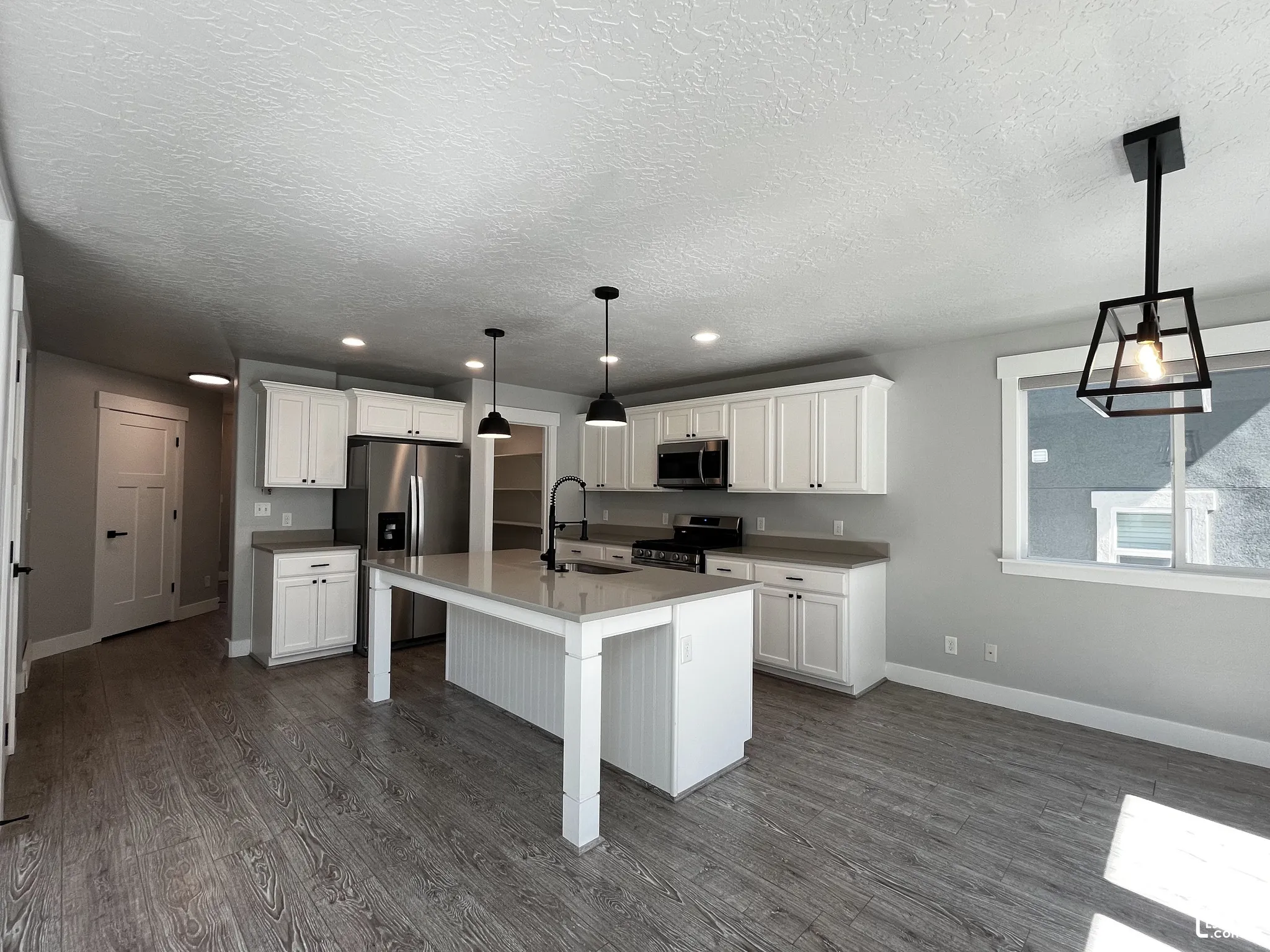 Open-concept kitchen with white shaker cabinetry, stainless steel appliances, a center island with pendant lighting, and wood-finish flooring