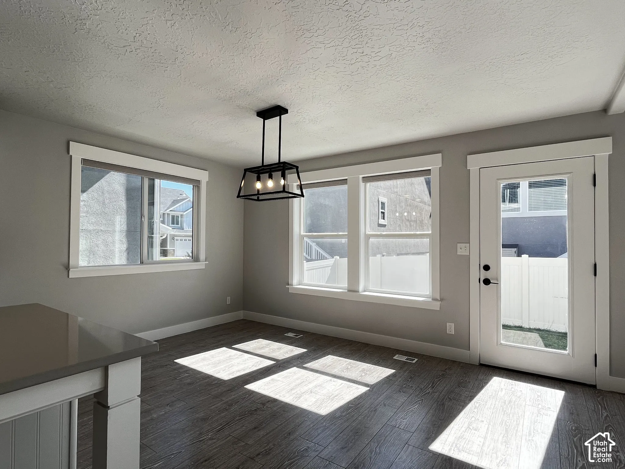 Wood-finish flooring with a contemporary black metal chandelier and multiple windows