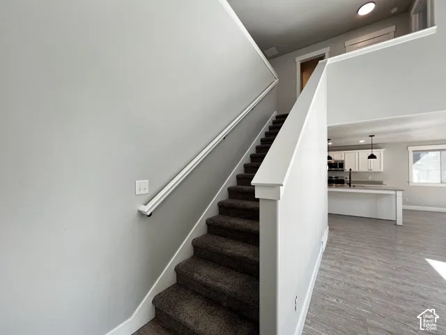 Carpeted staircase with white handrail, recessed lighting, wood-finish flooring, and white kitchen cabinetry