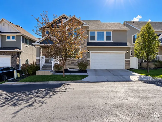 Stone and stucco exterior with a prominent two-car garage, concrete driveway, and covered entry porch with white railings
