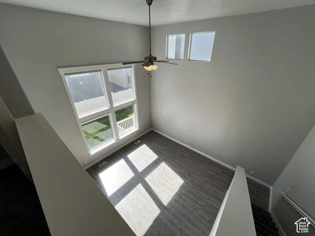 Double-height ceiling, large multi-pane windows, elevated windows, wood-finish flooring, and a ceiling fan with integrated lighting