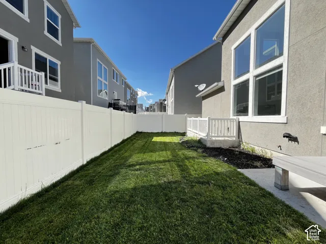 Spacious backyard featuring a manicured lawn, full-height privacy fencing, a ground-level patio, and a lower-level egress window with railing