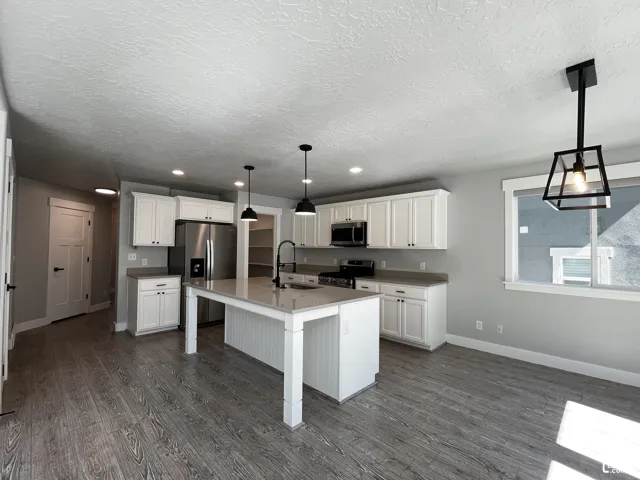 Open-concept kitchen with white shaker cabinetry, stainless steel appliances, a center island with pendant lighting, and wood-finish flooring