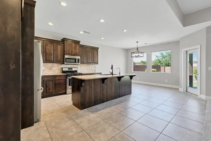 Kitchen featuring dark wood-finish cabinetry, stainless steel appliances, a center island with countertop, and tile flooring