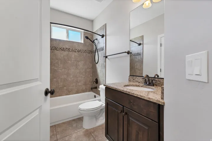 Full bathroom featuring a shower-over-tub with tiled surround, a vanity with a stone countertop and integrated sink, and dark wood-finish cabinetry