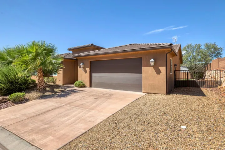 Stucco exterior with a tiled roof, an attached garage, a concrete driveway, and rock landscaping