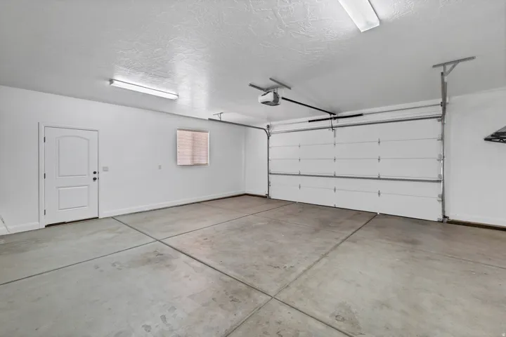 Concrete flooring, automatic garage door opener, white interior walls, overhead strip lighting, solid entry door