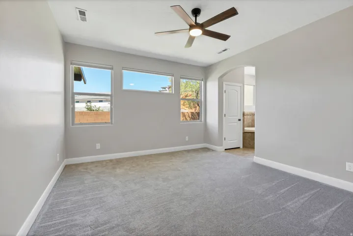 Spacious room featuring neutral carpeting, multiple windows, a ceiling fan, and an arched doorway leading to a tiled area