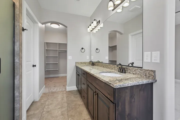 Dual vanity with granite countertop, integrated sinks, dark wood-finish cabinetry, and a large mirror with overhead lighting