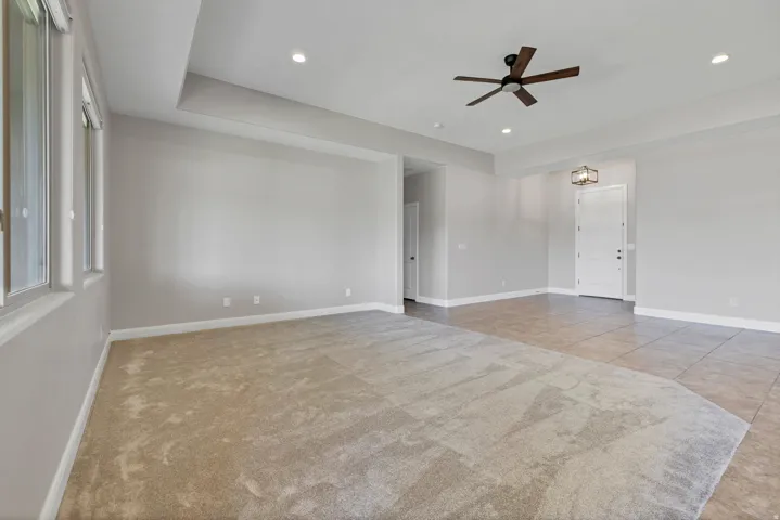 Recessed lighting, ceiling fan, tray ceiling, multiple windows, and a combination of carpet and tile flooring