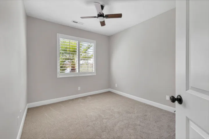 Carpeted flooring, window with plantation shutters, ceiling fan with light fixture, and panel door