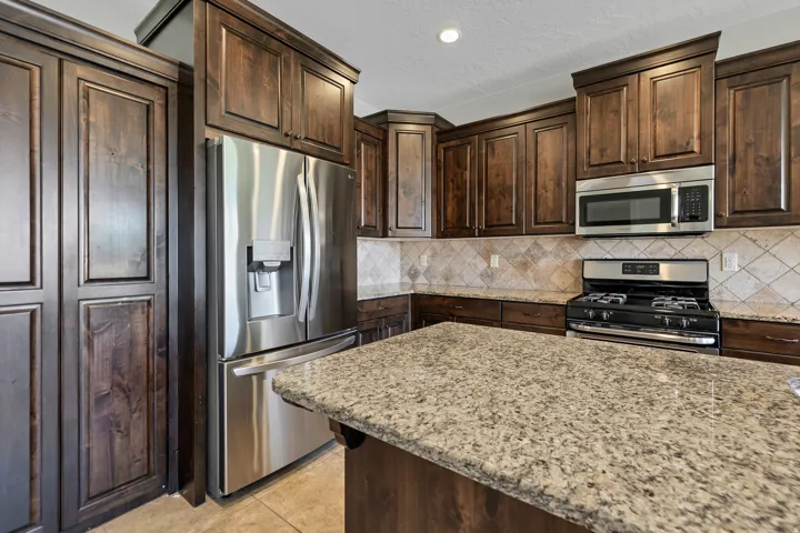 Kitchen featuring dark wood cabinetry, stainless steel appliances, a tile backsplash, and a large central island with a stone countertop