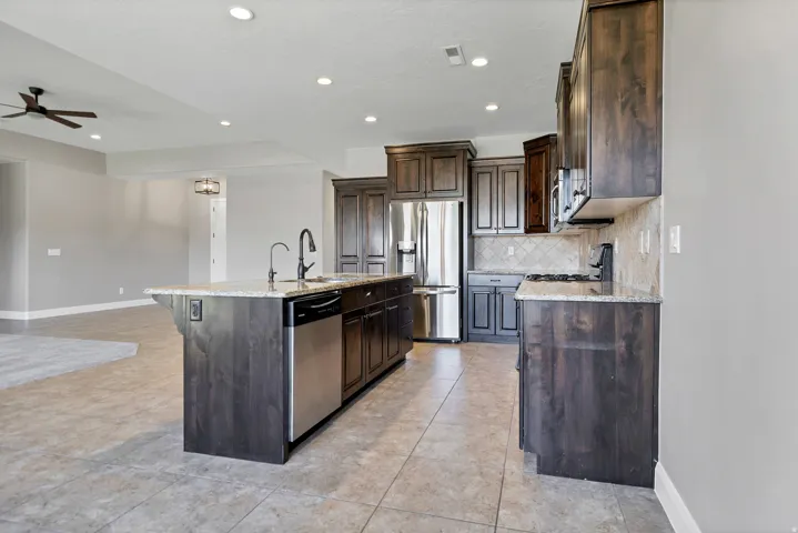 Kitchen featuring dark wood-finish cabinetry, stainless steel appliances, granite countertops, and tile flooring