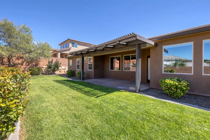 Expansive backyard featuring a covered patio with a slatted pergola, a concrete patio surface, and a manicured lawn