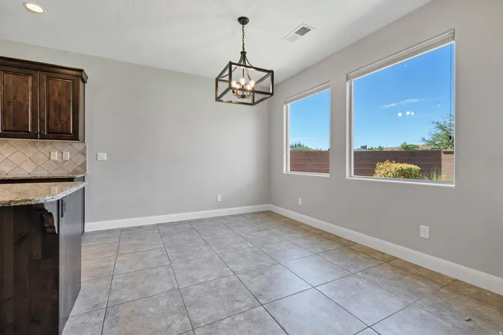 Tile flooring throughout, dark wood-finish cabinetry, granite countertop, neutral tile backsplash, and two expansive windows