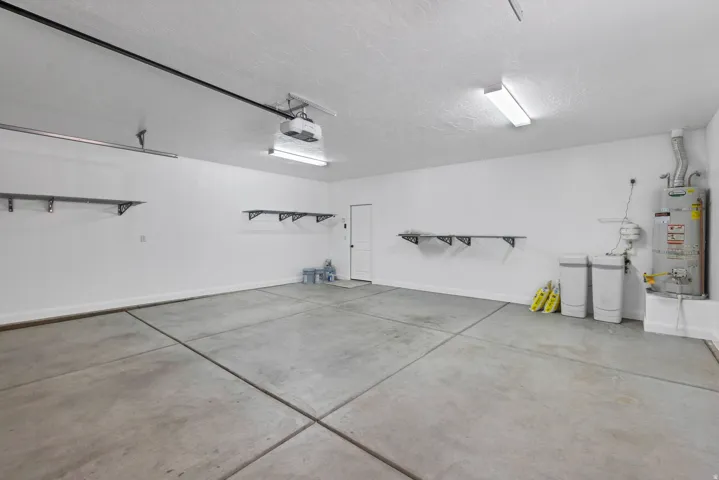 Concrete flooring, wall-mounted shelving brackets, fluorescent lighting, and a garage door opener