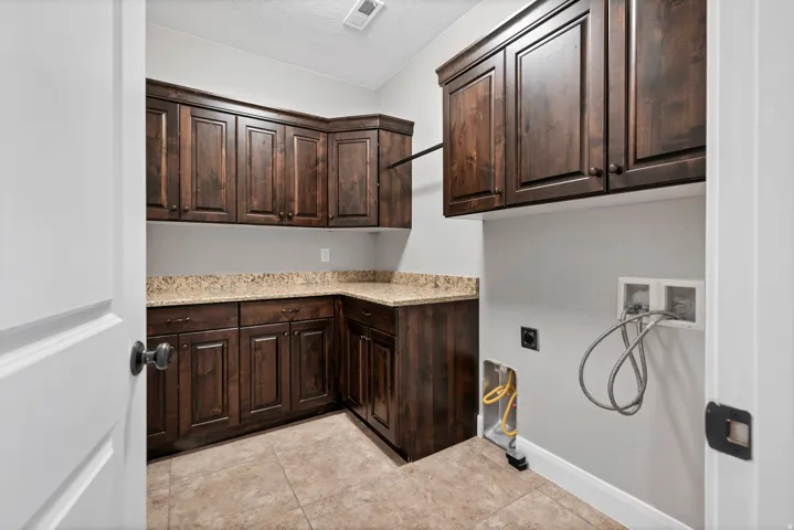 Wood-finish cabinetry with stone-finish countertops, tiled flooring, and a dedicated utility area