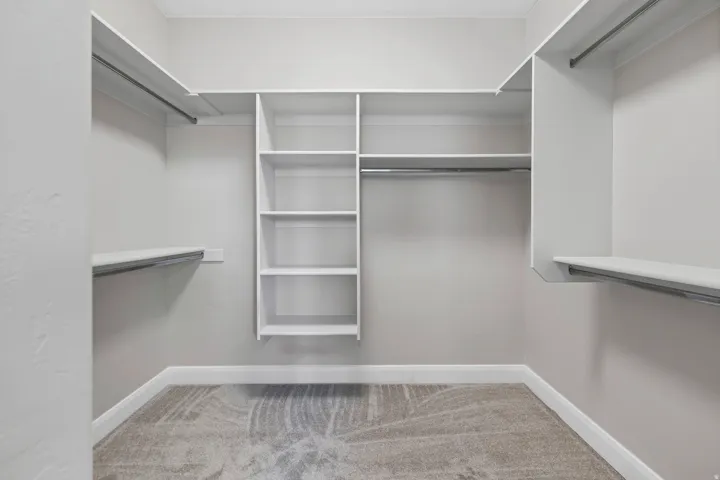 Walk-in closet featuring built-in shelving, multiple hanging rods, and neutral-toned carpeting